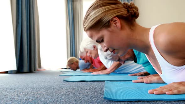 Trainer assisting senior citizens in practicing yoga