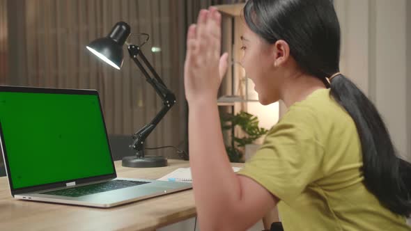 Asian Kid Girl Sitting In A Wheelchair While Video Call On Laptop With Mock Up Green Screen At Home
