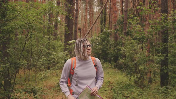 A Traveling Man with Dreadlocks with a Map in the Forest