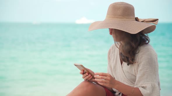 A Young Woman in a Big Straw Hat Using Her Smartphone