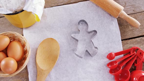 Butter paper, flour, rolling pin cookie cutter and eggs kept over a wooden table