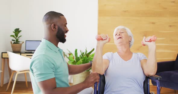 Video of happy african american male physiotherapist exercising with caucasian senior woman