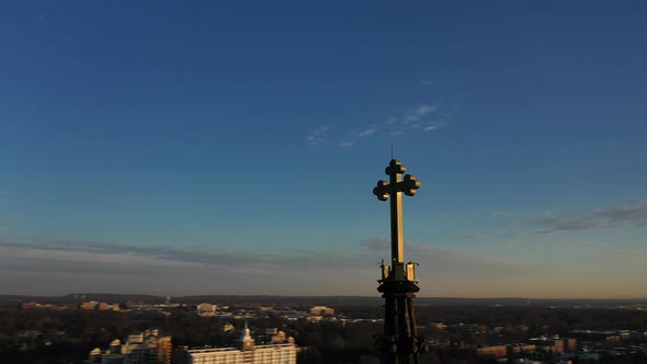 An aerial shot of a cathedral's steeple with a cross on it during at sunrise. The camera truck left