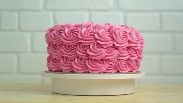 A beautiful cake with pink rosettes rotates on a pastry stand.