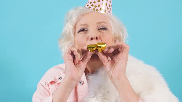 Happy Mature Woman in Party Hat Making a Noise in the Party