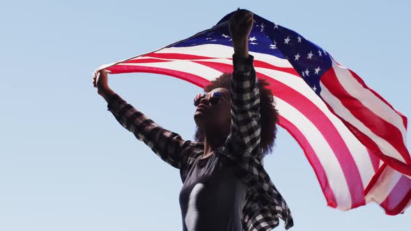 African american woman wearing sunglasses holding american flag up in the air