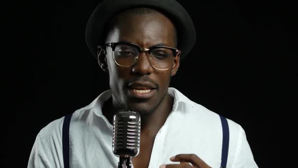 Man Young African American Singing Into a Microphone in a Recording Studio. Black Background. Close