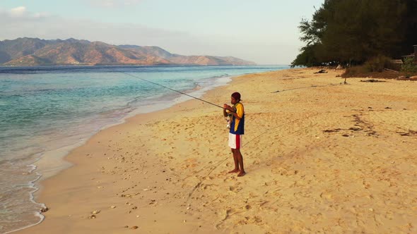 Man alone happy and fishing on luxury coastline beach voyage by blue water and white sand background