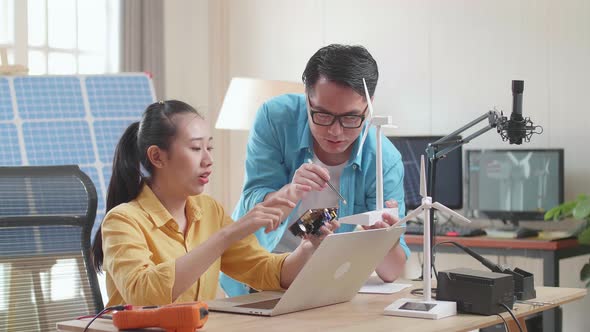 Asian Man And Woman Discuss About Work With Circuit Board, Wind Turbine And Laptop Computer