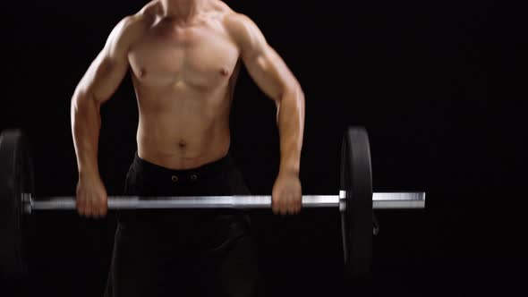 Man is Doing Exercises with a Barbell is Engaged in a Crossfit on a Black Background in the Studio