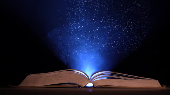 In a Dark Smoky Studio a Thick Open Book Lies on a Table Against a Black Background