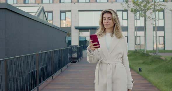 Female Beautiful Person Using Smartphone While Walking at City Street. Cheerful Young Woman Touching