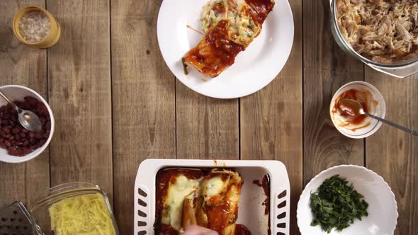 Top View of a Plate with Ready Enchilada Standing Among Ingredients and Man Hands Putting It
