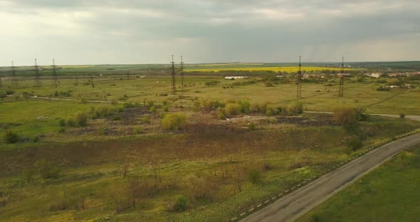 Large Pylons Of Power Lines On A Green Field, Long Road, In The Afternoon, In Spring