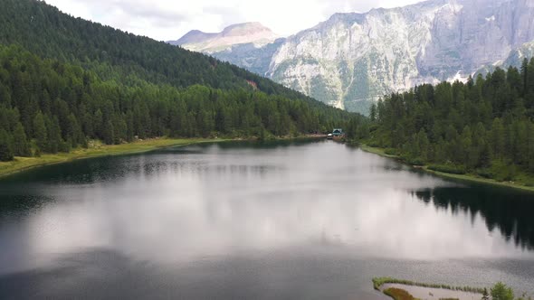 Aerial View Of A Mountain Lake In The Dolomites With Refuge Among Firs And Mountains