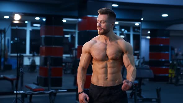 Muscle athlete strongman pumps muscules in a gym after heavy training. Perfect torso with strong abs