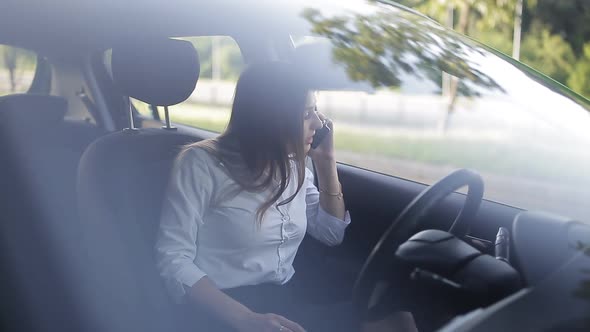 Businessman Communicates By Phone at the Wheel of the Car and Makes Notes in His Diary