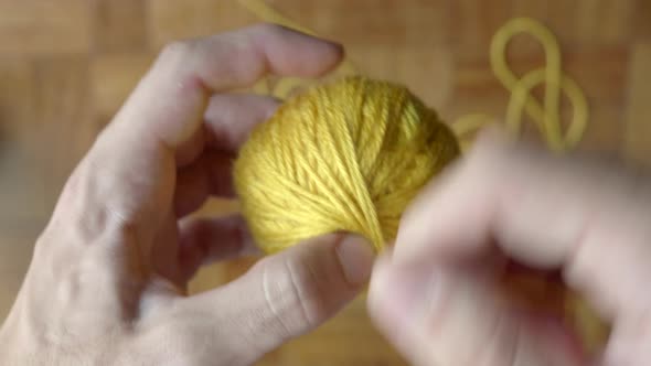 Hand finishing winding ball of yellow wool. Static blur background. Top view