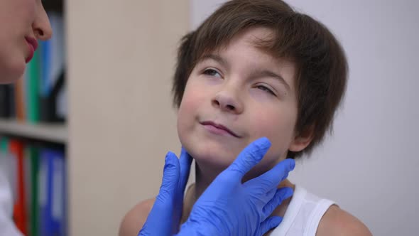 Closeup Sad Caucasian Ill Boy Sitting in Hospital As Woman Touching Neck Checking Glands