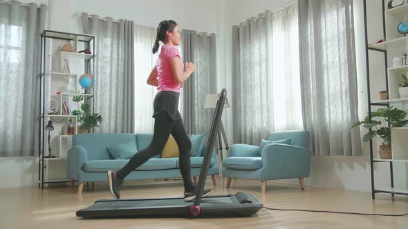 Side View Of Asian Woman Running On A Treadmill At Home