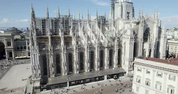 Ornate exterior of famous Milan Cathedral with tourists roaming about; aerial