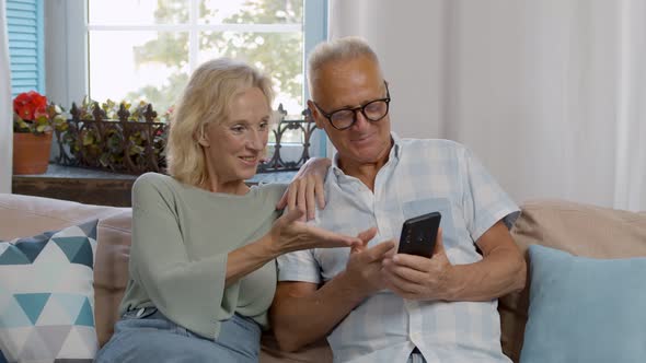 Happy Elderly Couple Relax on Couch Using Cellphone