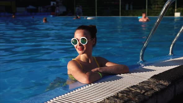 A Beautiful Woman in Stylish Glasses is in the Pool She Enjoys a Warm Day