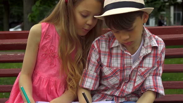 Children Draw in the Album Together on the Bench