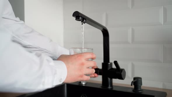 Unrecognizable man pouring drinking water into transparent clean glass from tap