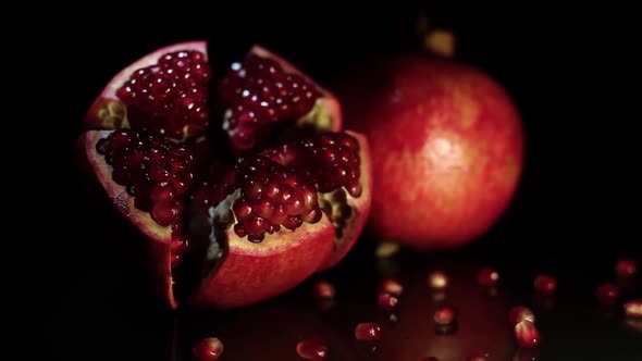 Two Fruit Pomegranates Rotate on a Black Table on a Black Background