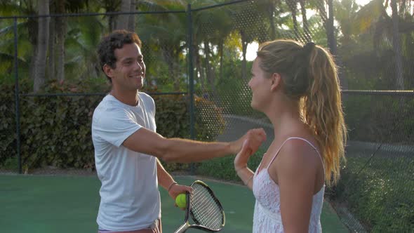 A boyfriend teaching his girlfriend how to play tennis while on vacation.