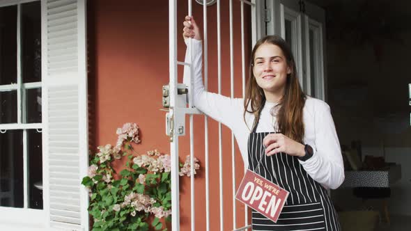 Smiling caucasian waitress standing in door, holding open sign, looking at camera