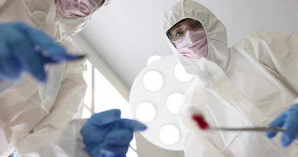 Two Doctors Wearing Masks and Protective Suits Hold Scalpel and Forceps with Swab of Blood  Movie