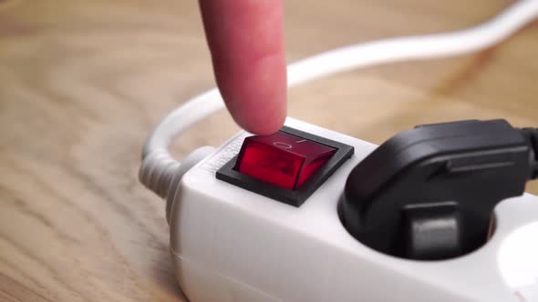 Disconnecting an electrical power strip by pressing a red switch close up. Connected black plug