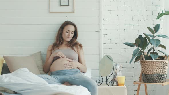 Beautiful Pregnant Woman Touching Belly in Bedroom. Dreaming Expectant Mother