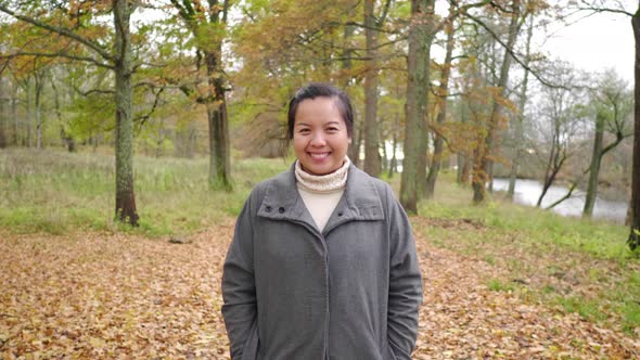 Front view of Asian woman standing and smiling in forest Autumn season