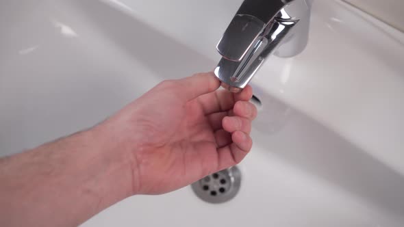 Man's hand dismantles the faucet and unscrews the filter for cleaning in the white bathroom sink