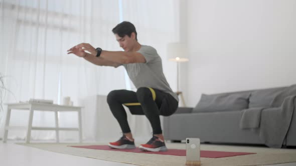 Young Man Athlete Exersices With Resistance Band. Fitness Trainer Doing Stretching Squats With