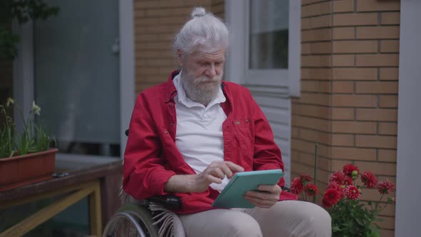 Portrait of Handicapped Bearded Senior Caucasian Man Surfing Social Media on Tablet in Slow Motion