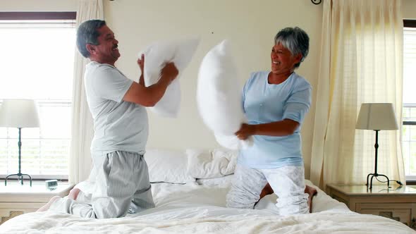 Senior couple having pillow fight on bed 4k