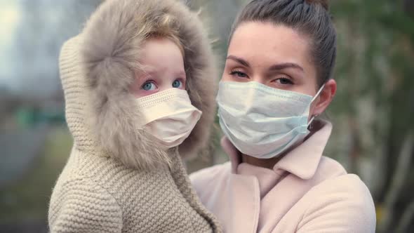 young mother and little daughter in medical masks on the street