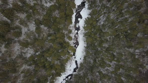 Top down aerial shot of drone going up above snowy river in winter