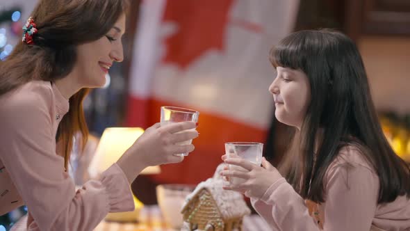 Side View Mother Kissing Daughter on Christmas Eve Toasting Clinking Glasses Drinking Milk at Home