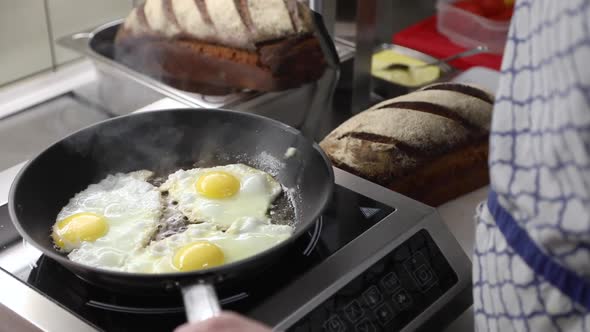 Chef Frying Three Eggs On Skillet Pan With Loaves Of Bread On The Side. - close up
