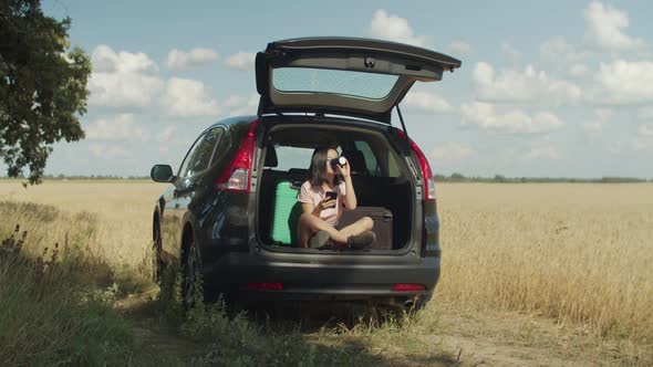 Asian Woman Networking on Phone in Car Trunk