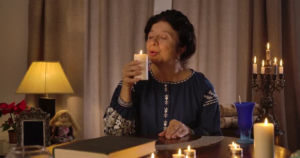 Portrait of Caucasian Female Magician Blowing Out Candle and Putting It on the Table. Smiling Mature