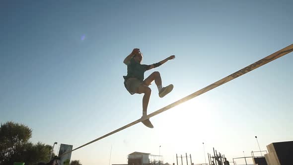 Slow-motion Shooting of a Young Man Balancing on a Slackline in a Public Park, Shooting Against the