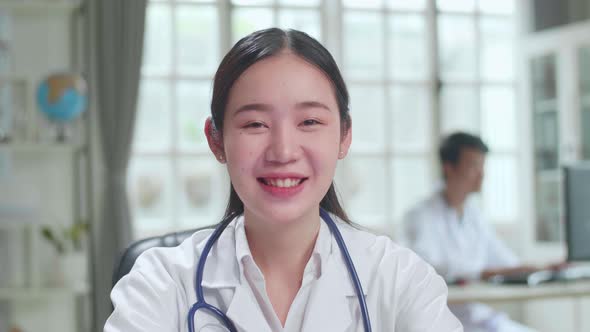 Asian Female Doctor Physician In White Medical Uniform Speaking to Camera During Video Conference