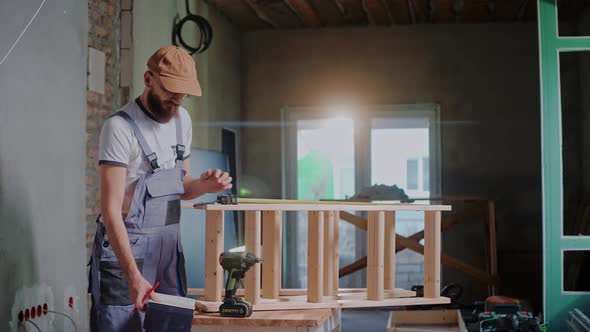 Male Builder Uses a Tape Measure to Measure Wood Construction and Writes Notes