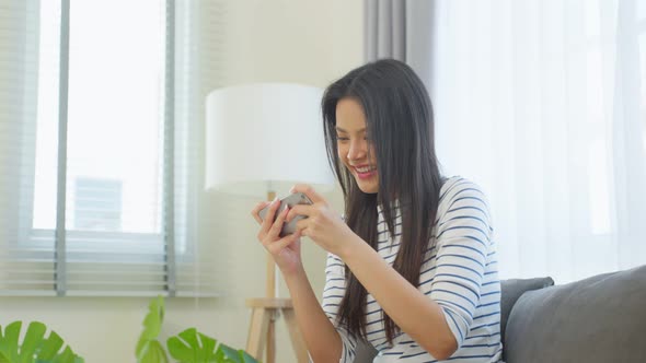 Asian young beautiful woman playing mobile game on smartphone at home